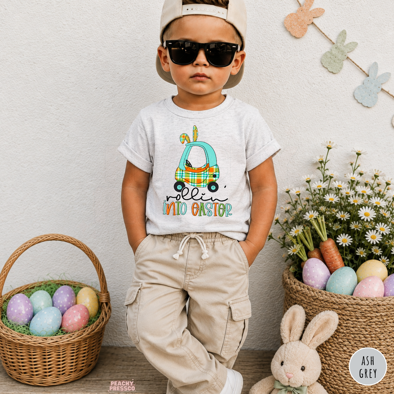 Toddler boy wearing an ash grey Rollin Into Easter Easter shirt with a blue plaid bunny car design and Easter bunny ears.