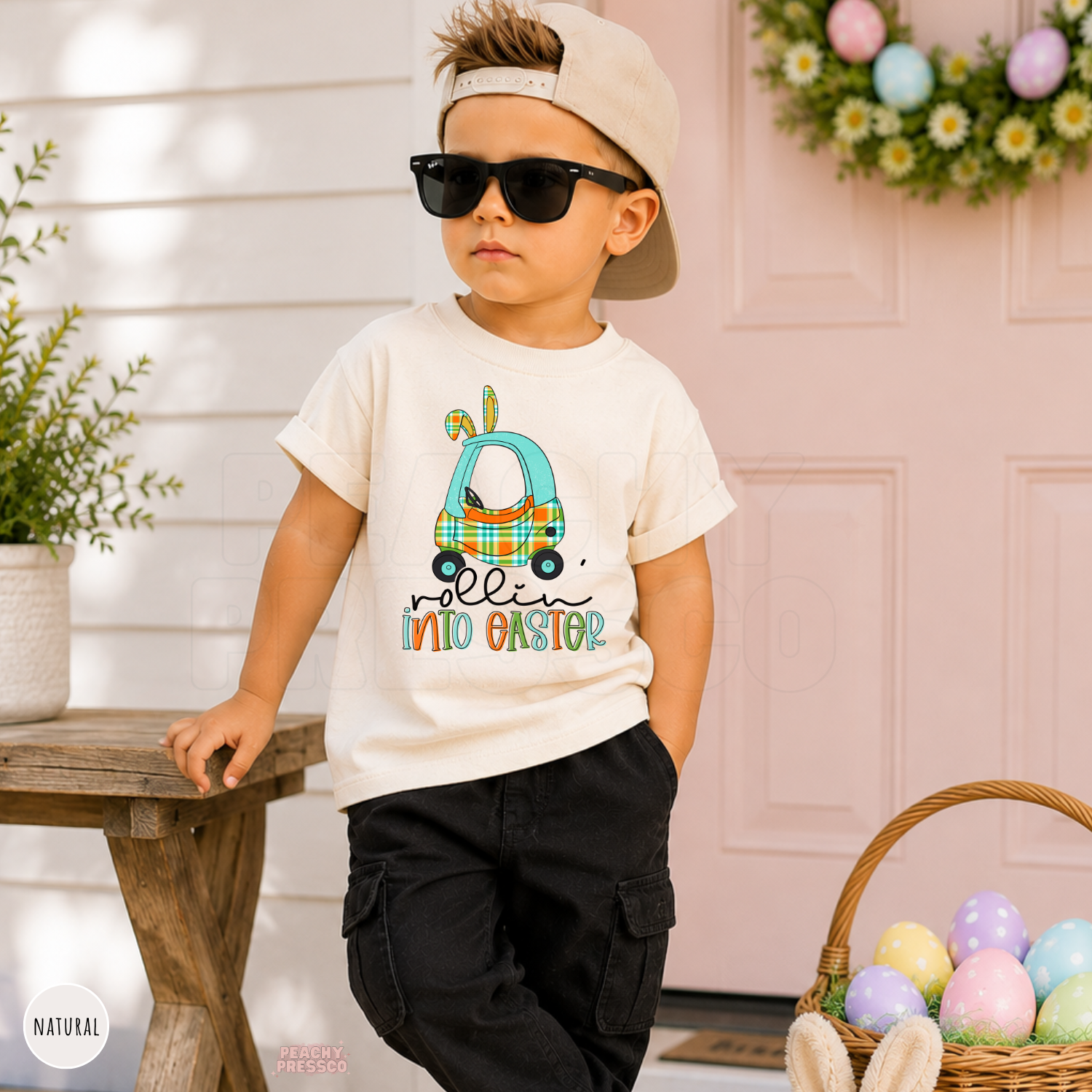 Toddler boy wearing a natural Rollin Into Easter shirt featuring a blue plaid bunny car graphic for Easter.