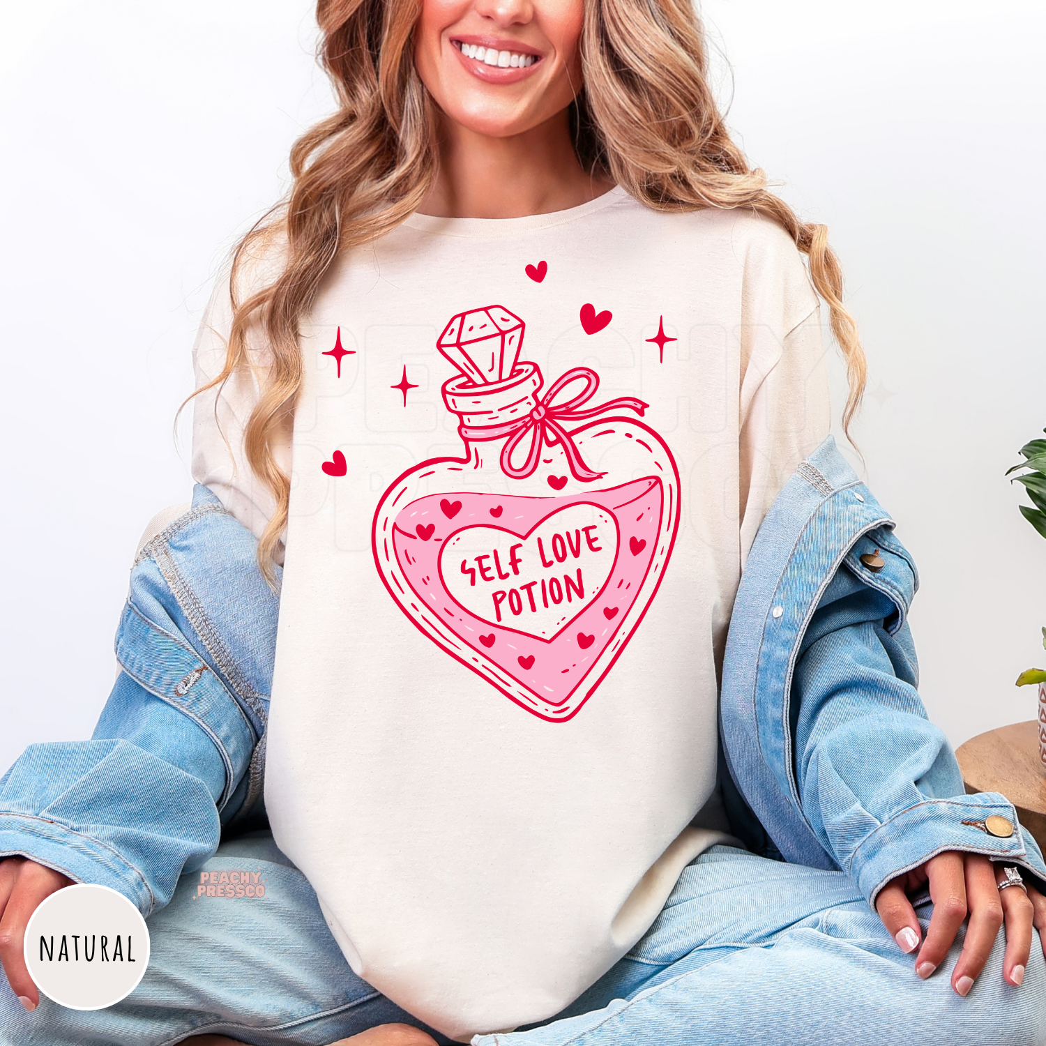 Natural shirt showcasing a heart-shaped Self Love Potion bottle graphic with playful hearts and sparkles in vibrant pink.