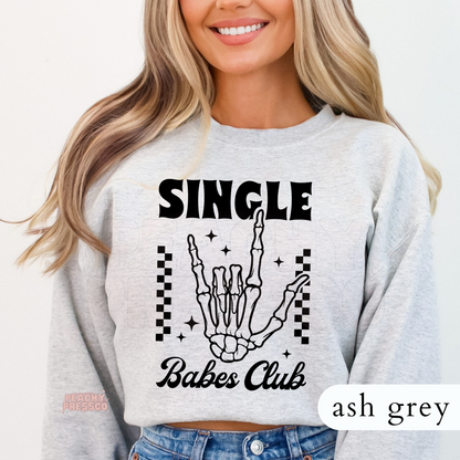 Ash grey crewneck sweatshirt with a bold "Single Babes Club" skeleton hand graphic, retro typography, and checkerboard accents for a cute anti-Valentine style.
