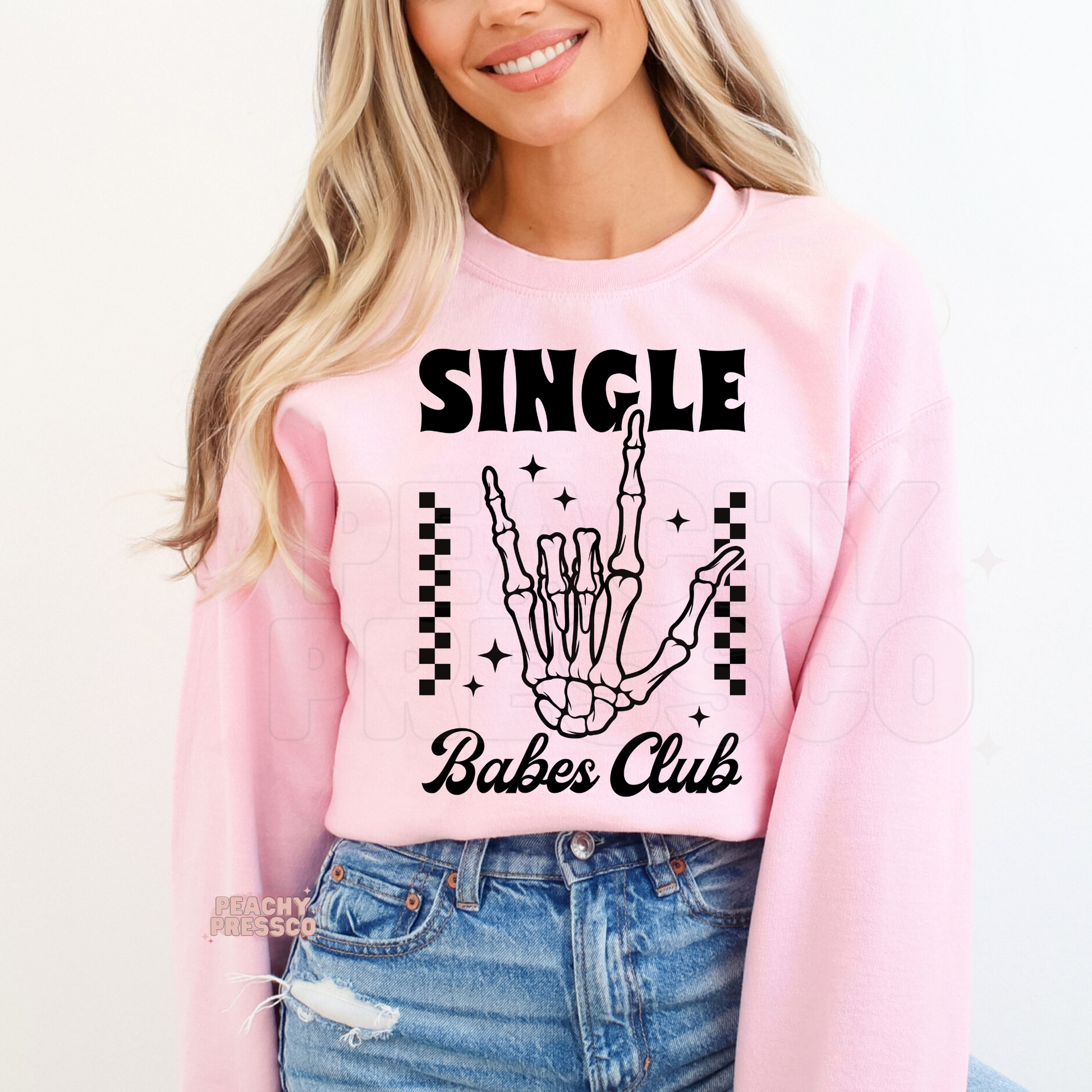 Light pink crewneck sweatshirt featuring a "Single Babes Club" skeleton hand graphic with retro lettering, checkerboard details, and fun Valentine's-inspired style.