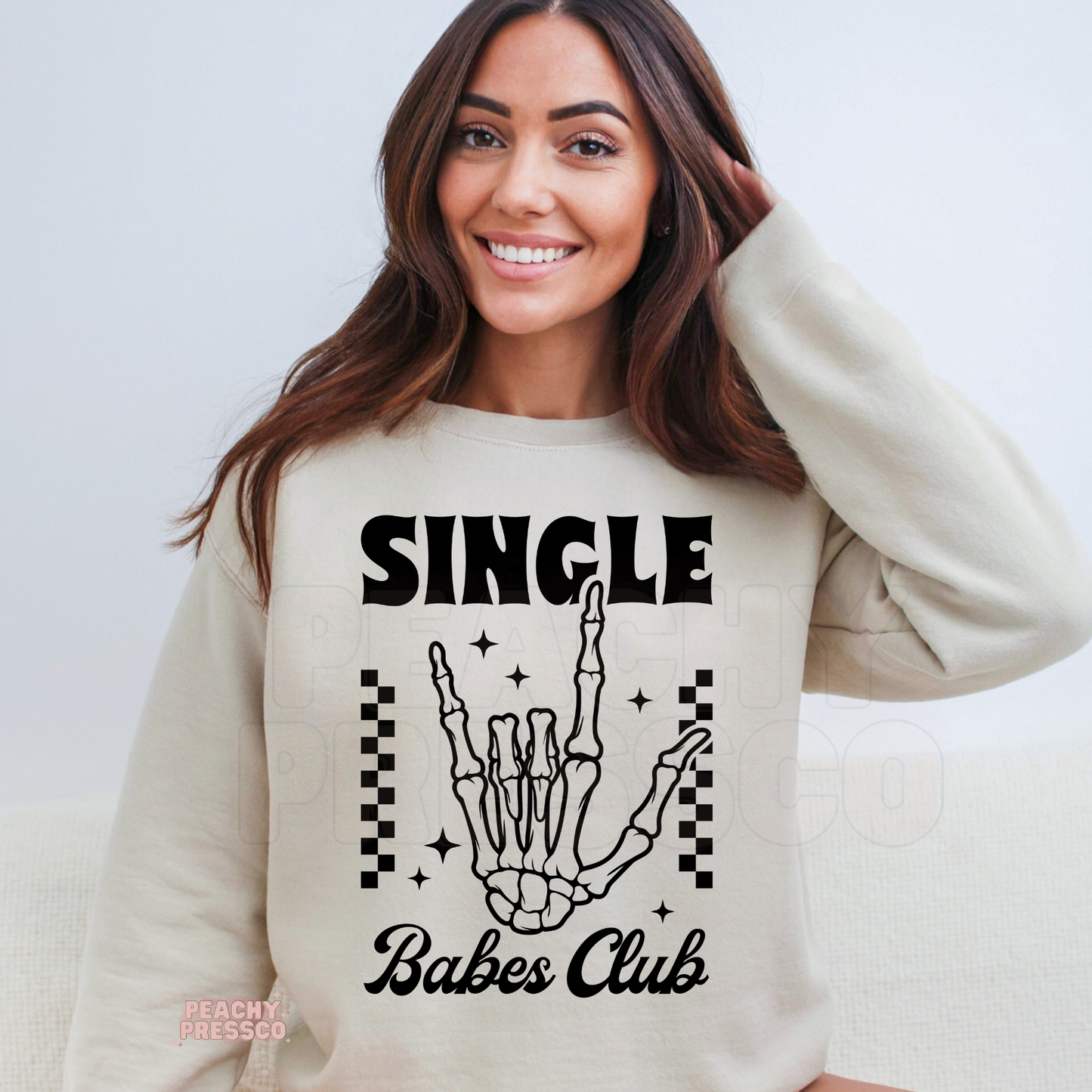 Sand crewneck sweatshirt showcasing a stylish "Single Babes Club" skeleton hand graphic with vintage-inspired lettering and black checkerboard accents.