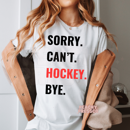 White unisex t-shirt featuring the "Sorry. Can't. Hockey. Bye." graphic with bold red hockey lettering.