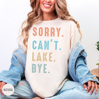 Natural shirt featuring the humorous "Sorry. Can't. Lake. Bye." graphic in vintage-inspired peach, blue, and mustard distressed typography.