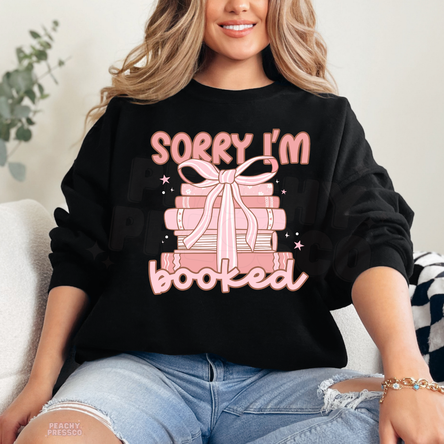Black crewneck sweatshirt featuring a pink stack of books with a bow and "Sorry I'm Booked" graphic, a cute gift for book lovers.