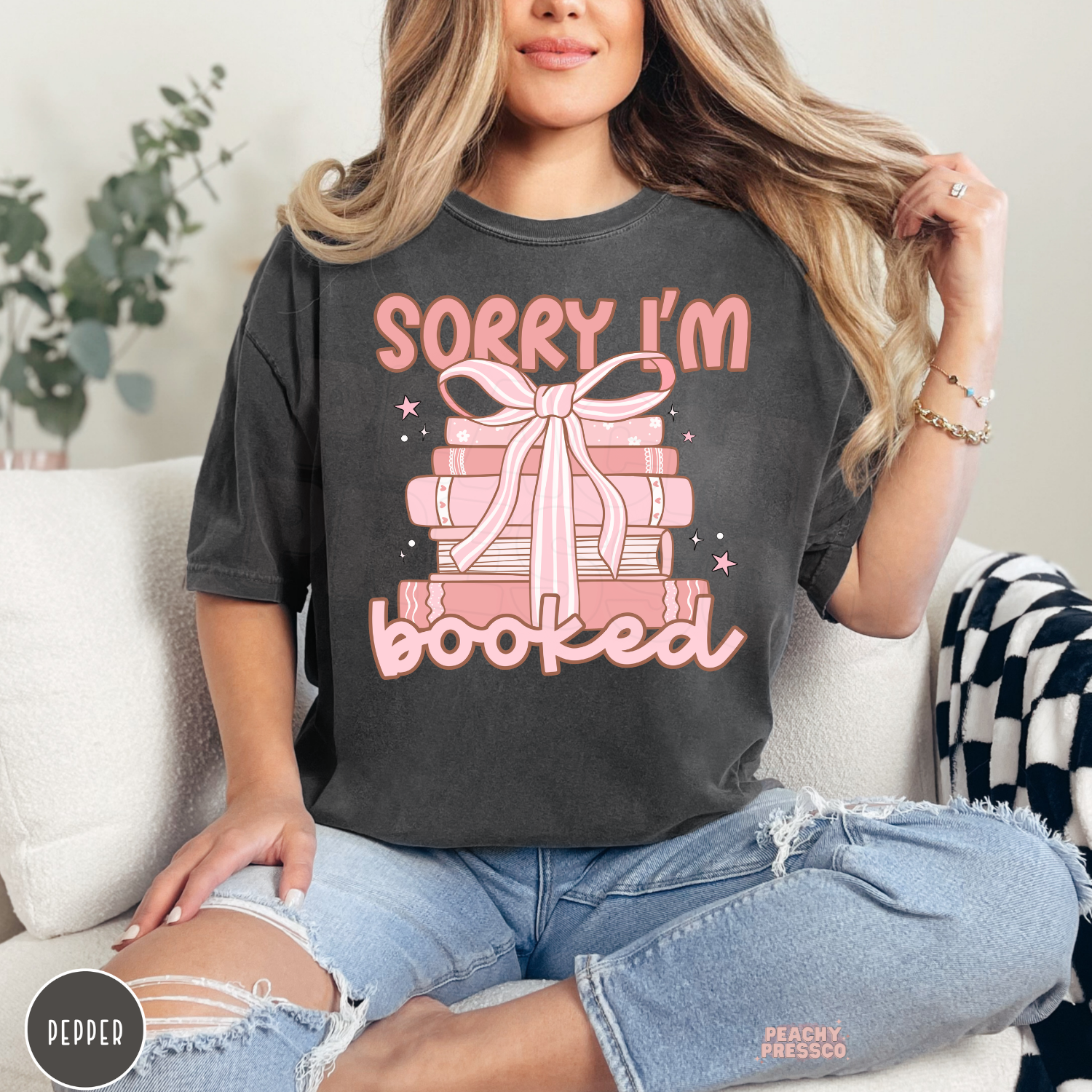 Pepper Comfort Colors tee featuring a pink stack of books tied with a bow and the phrase "Sorry I'm Booked" for bookworms and readers.