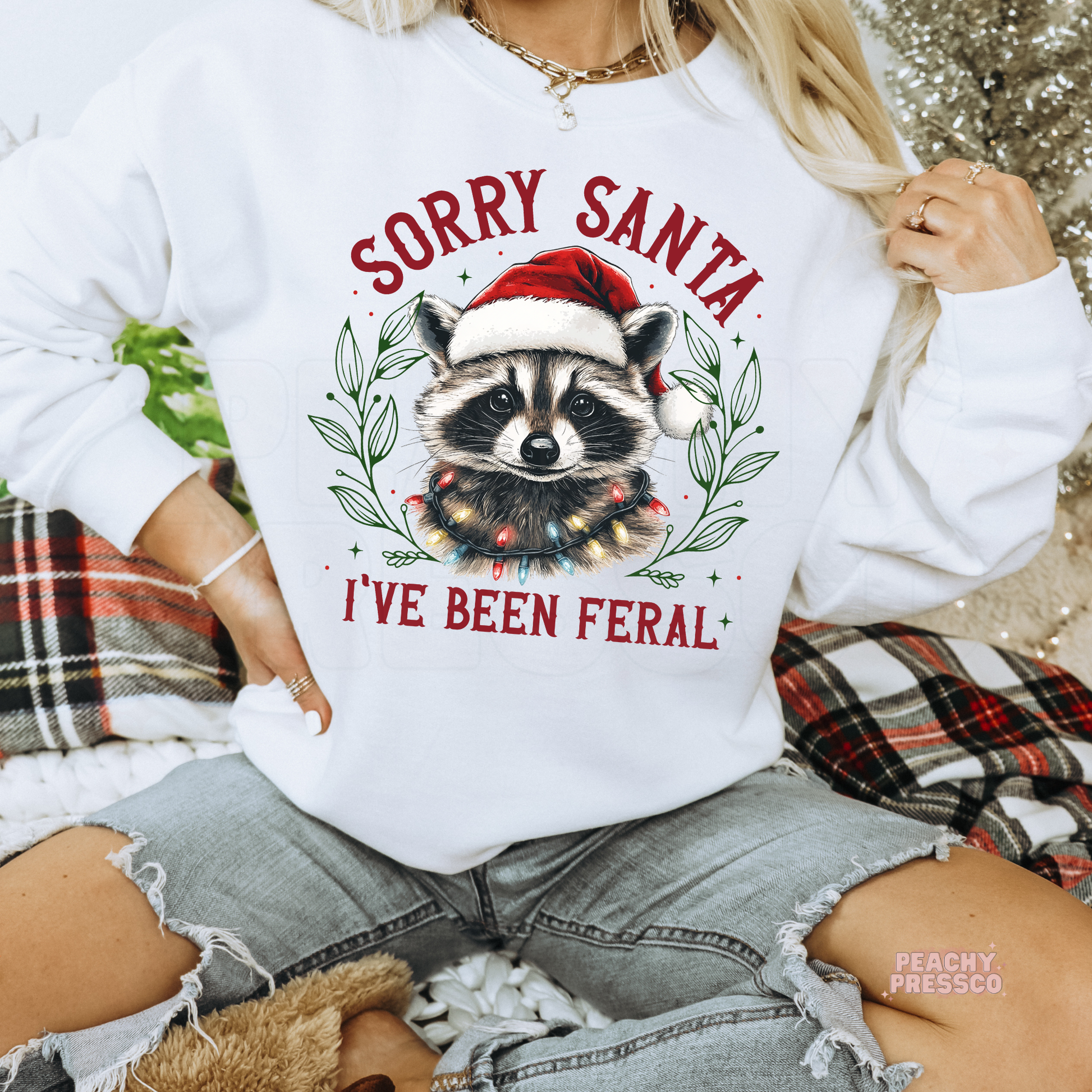 Women wearing a white crewneck sweatshirt with a funny Christmas raccoon wrapped in lights, styled with ripped denim jeans.