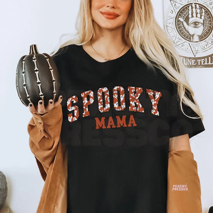 Woman wearing a black Spooky Mama Halloween graphic t-shirt while holding a black skeleton pumpkin.