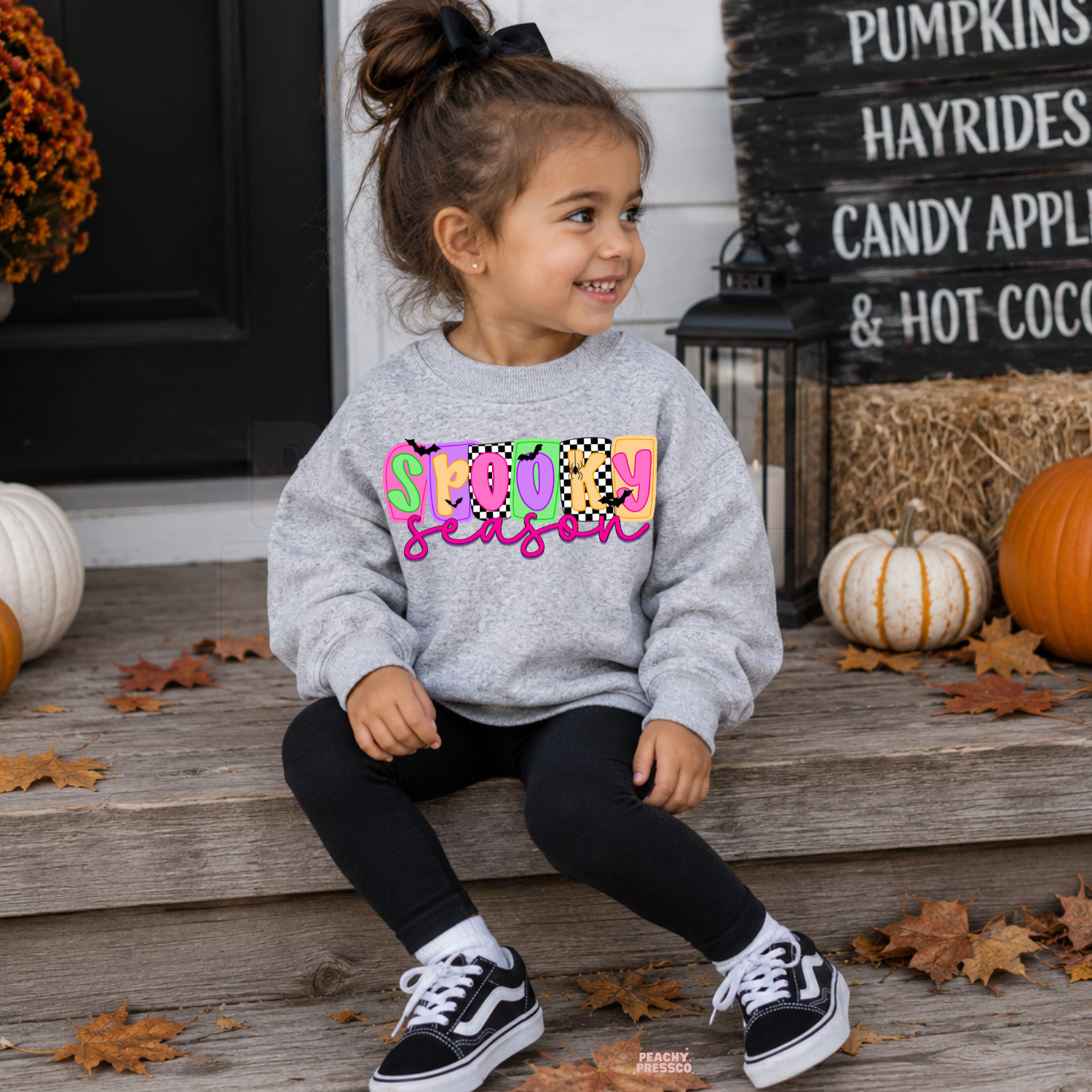Girl wearing a sport grey Spooky Season Halloween sweatshirt featuring a bright colorful graphic in a festive pumpkin setting.