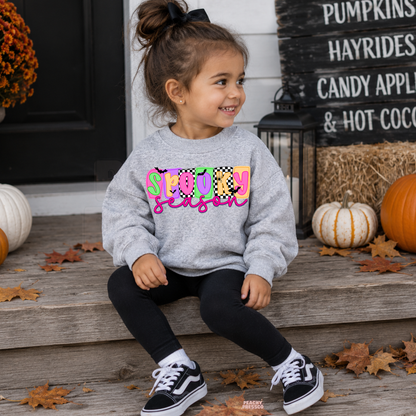 Girl wearing a sport grey Spooky Season Halloween sweatshirt featuring a bright colorful graphic in a festive pumpkin setting.