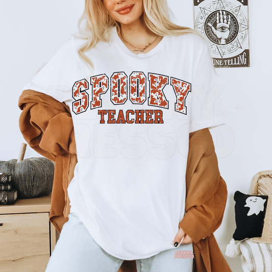 Woman wearing a white Spooky Teacher Halloween graphic t-shirt with distressed varsity ghost print for teachers.