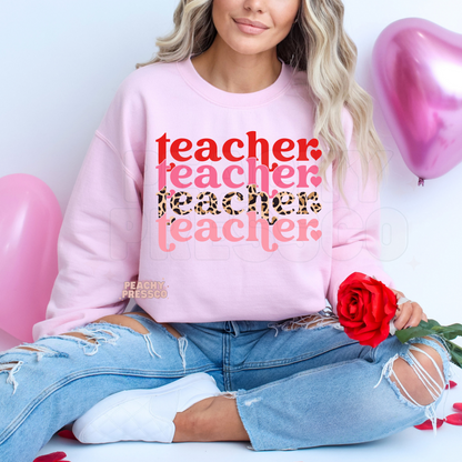 Pink sweatshirt displaying a stacked Valentine teacher design with retro typography, pink lettering, and leopard print accents.