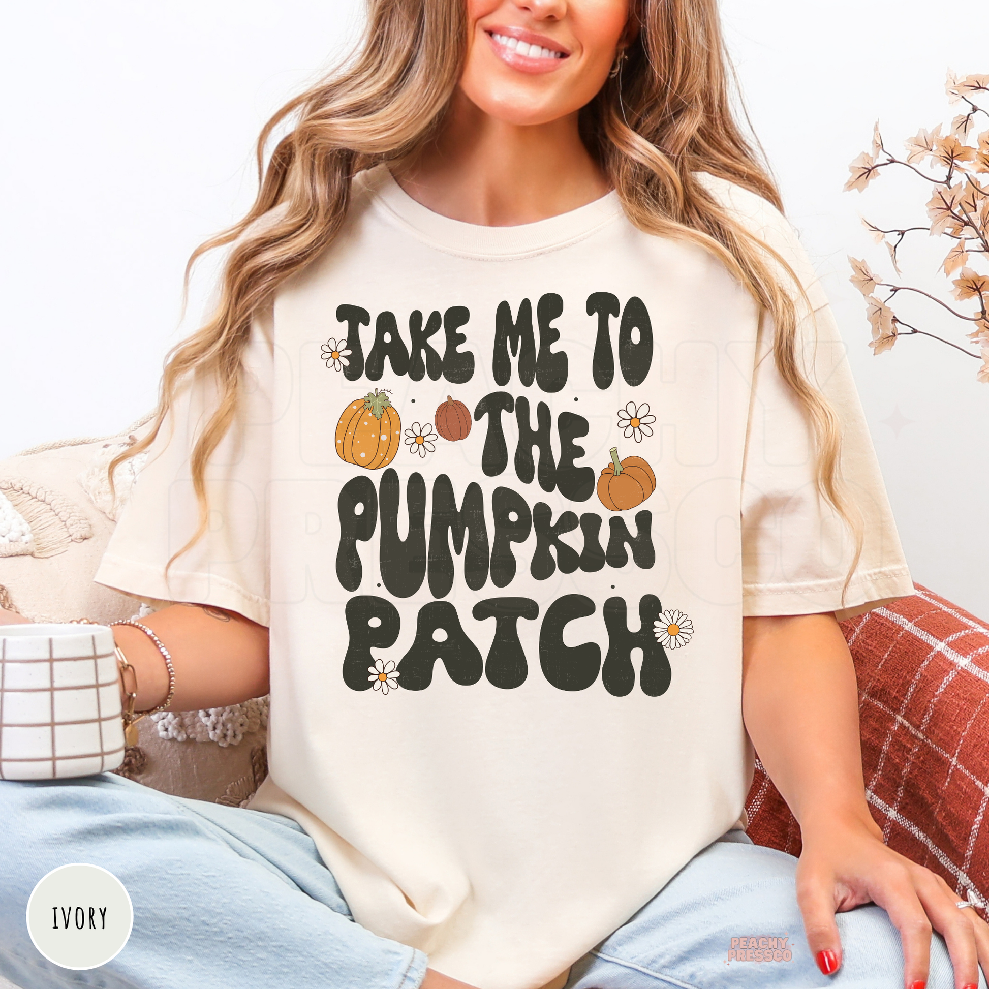 Woman wearing an ivory graphic t-shirt featuring a cute retro "Take Me to the Pumpkin Patch" design with pumpkins and flowers.
