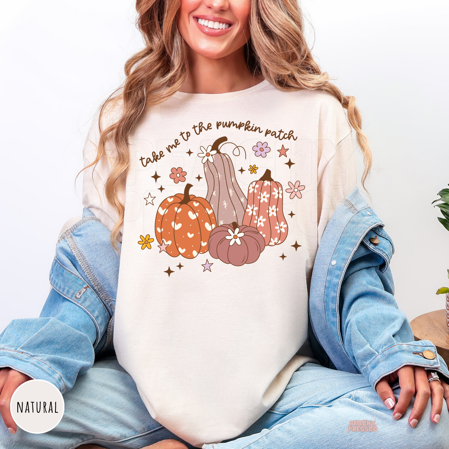 Woman wearing a natural shirt featuring a charming "Take Me To The Pumpkin Patch" graphic with floral pumpkins and whimsical fall accents, ideal for cozy autumn days and pumpkin patch visits.