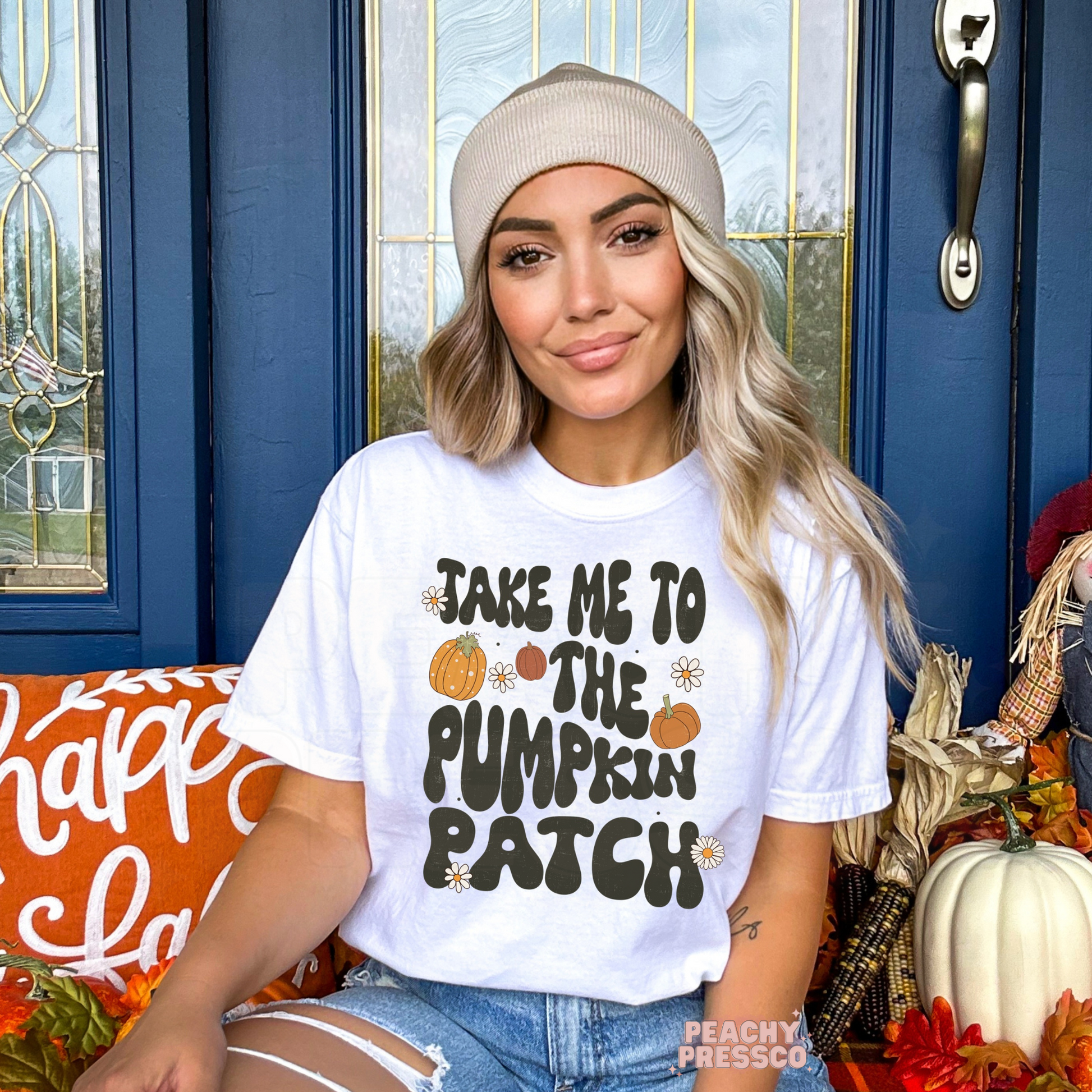 Woman wearing a white graphic t-shirt with the phrase "Take Me to the Pumpkin Patch" surrounded by pumpkins and daisies.