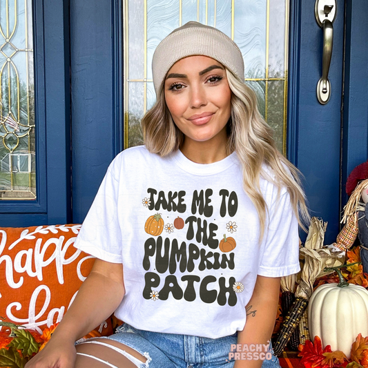 Woman wearing a white graphic t-shirt with the phrase "Take Me to the Pumpkin Patch" surrounded by pumpkins and daisies.