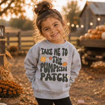 Smiling toddler girl wearing a sport grey "Take Me to the Pumpkin Patch" sweatshirt at a pumpkin patch with pumpkins, hay bales, and cozy autumn scenery.