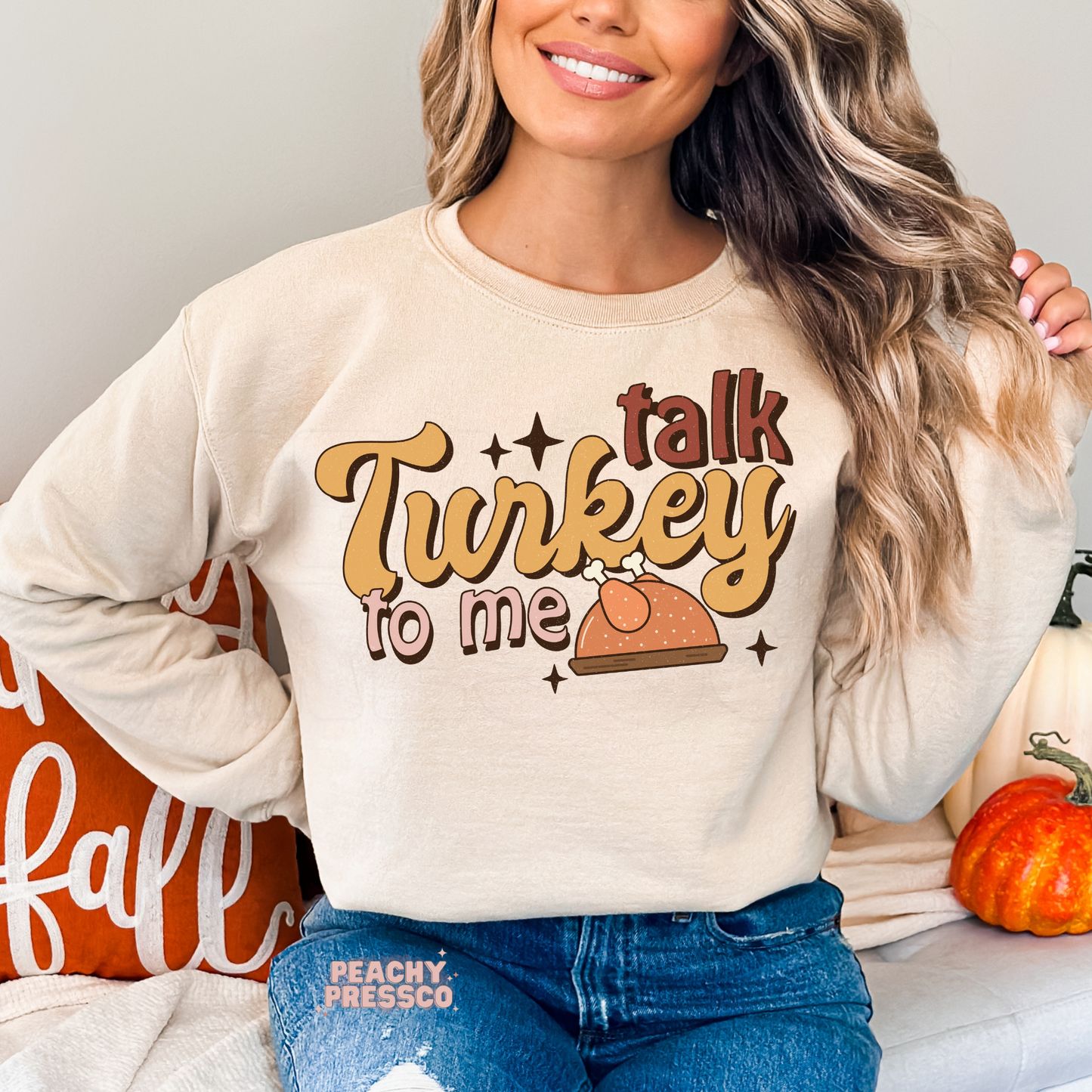 Woman wearing a sand crewneck sweatshirt featuring a retro "Talk Turkey To Me" Thanksgiving design with a roasted turkey illustration, perfect for fall gatherings, Friendsgiving, and cozy autumn outfits.