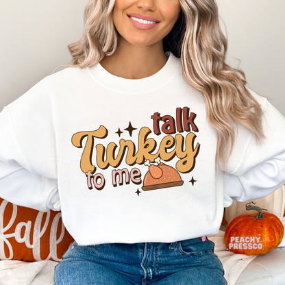 Woman wearing a white crewneck sweatshirt featuring a retro "Talk Turkey To Me" Thanksgiving design with a turkey illustration, a funny and cozy fall sweatshirt for Thanksgiving and Friendsgiving.