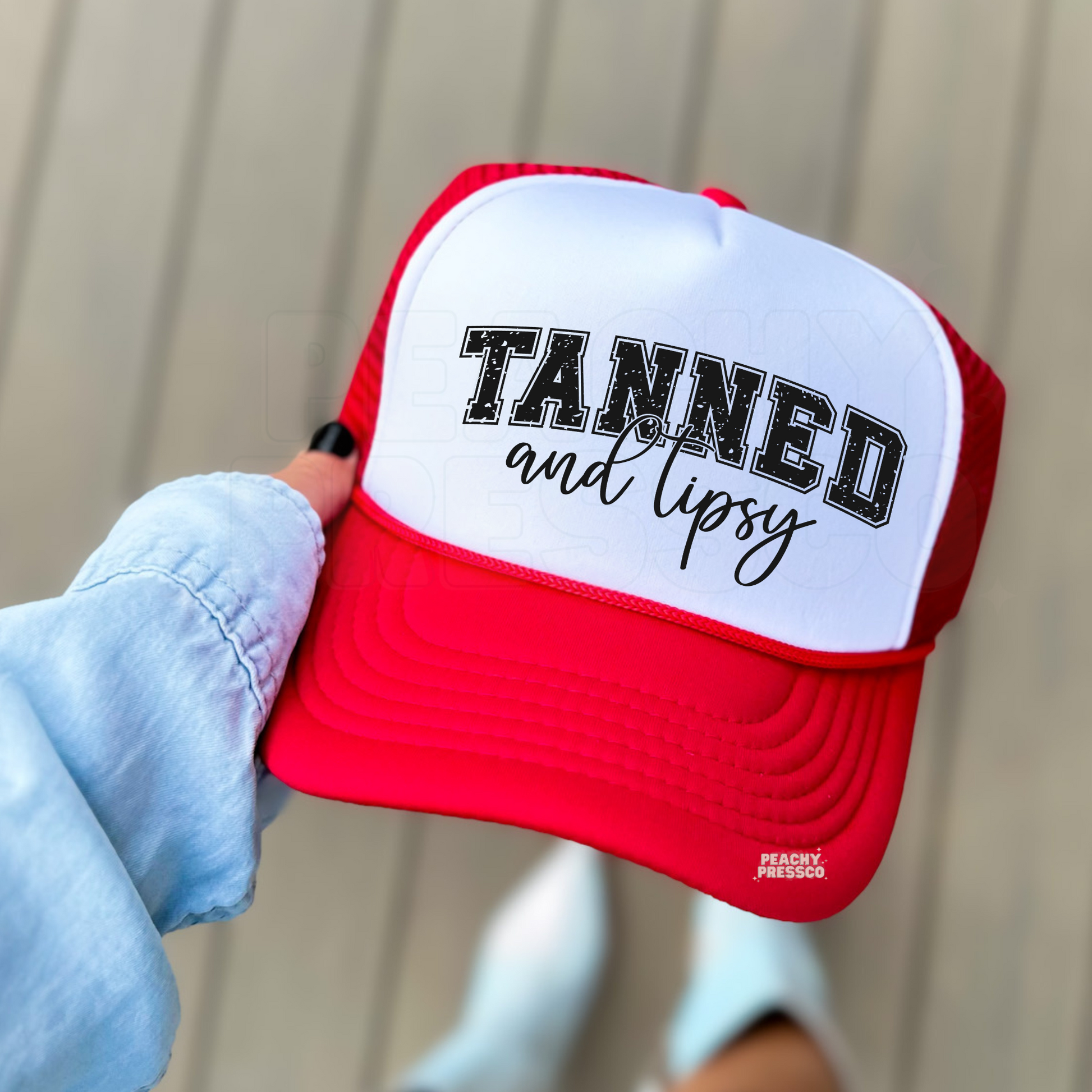 Red and white foam trucker hat featuring a distressed "Tanned and Tipsy" design in varsity lettering with script text. Fun beach trucker hat for summer vacations, lake weekends, boat days, girls' trips, and tropical getaways.