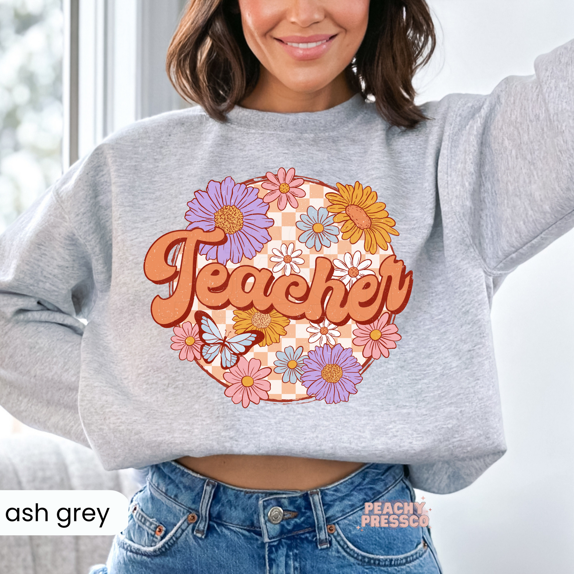 Ash grey teacher sweatshirt featuring a retro floral "Teacher" graphic with colorful flowers, butterfly, and checkerboard background.