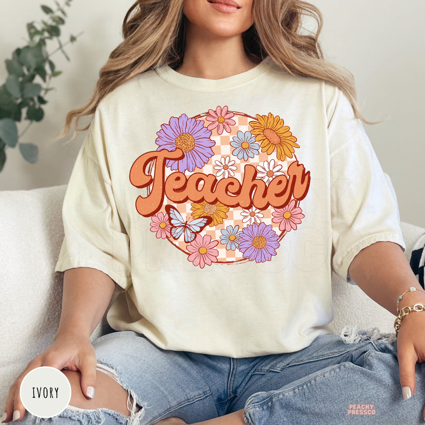 Ivory Comfort Colors teacher t-shirt featuring retro floral "Teacher" lettering with colorful flowers, butterfly, and peach checkerboard background.