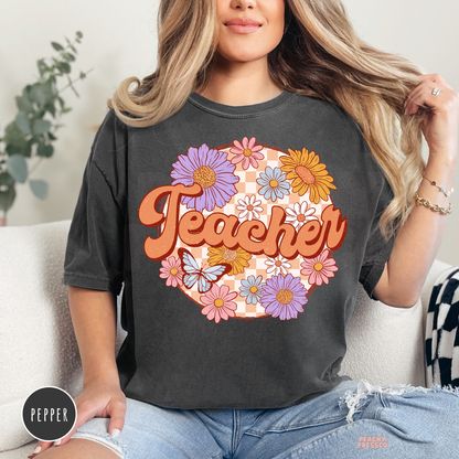 Pepper Comfort Colors teacher t-shirt featuring a retro floral "Teacher" graphic with colorful flowers, butterfly, and checkerboard background.