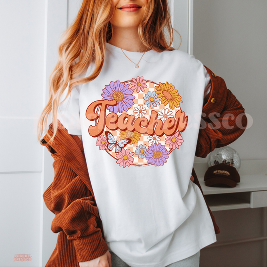 White teacher t-shirt featuring vintage floral "Teacher" design with pastel flowers, butterfly, and peach checkerboard background.