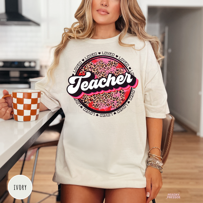 Ivory unisex t-shirt displaying a retro Teacher leopard print graphic with pink accents and Valentine's-themed typography.