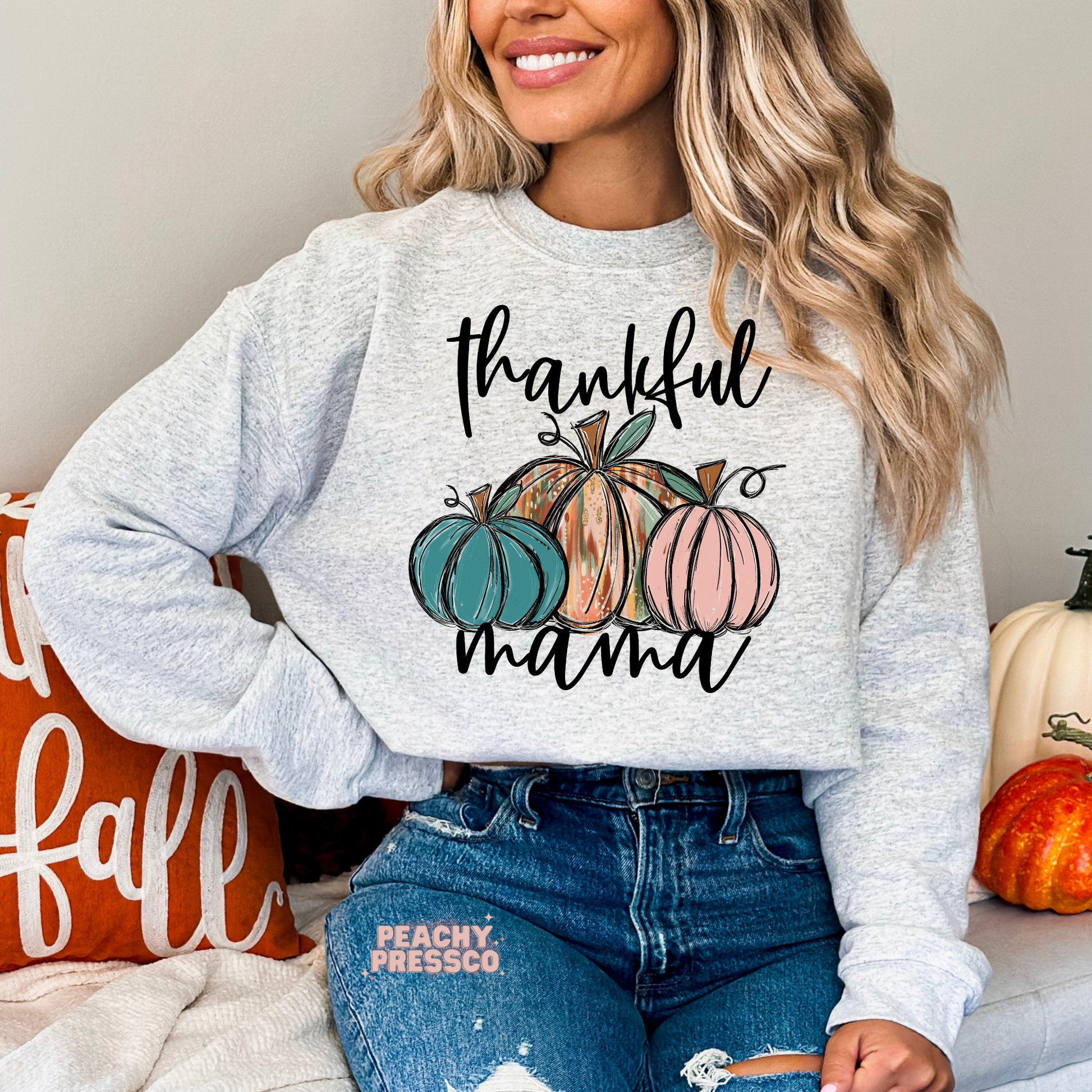 Woman wearing an ash grey crewneck sweatshirt featuring a "Thankful Mama" design with colorful pumpkins, a cozy Thanksgiving sweatshirt perfect for fall moms, pumpkin patch visits, and autumn gatherings.
