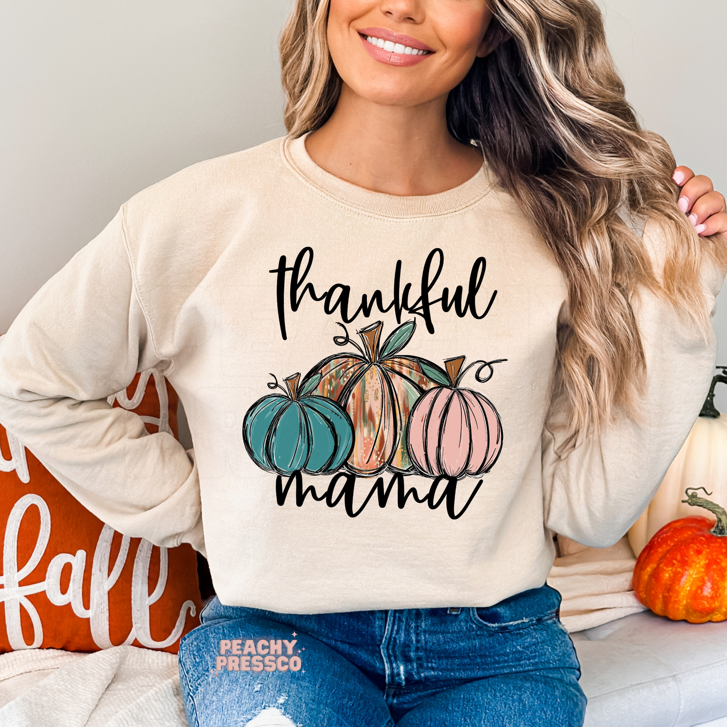 Woman wearing a sand colored crewneck sweatshirt featuring a "Thankful Mama" design with colorful pumpkins, perfect for Thanksgiving, pumpkin patch outings, and cozy fall style.