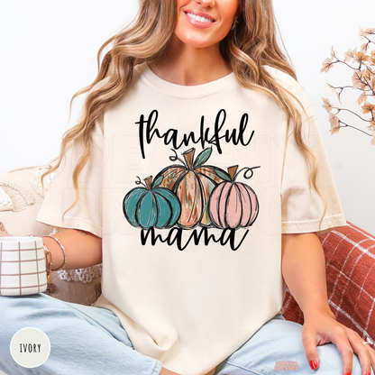 Woman wearing an ivory Comfort Colors t-shirt featuring a "Thankful Mama" pumpkin design with colorful pumpkins, perfect for autumn, pumpkin patch visits, and Thanksgiving.
