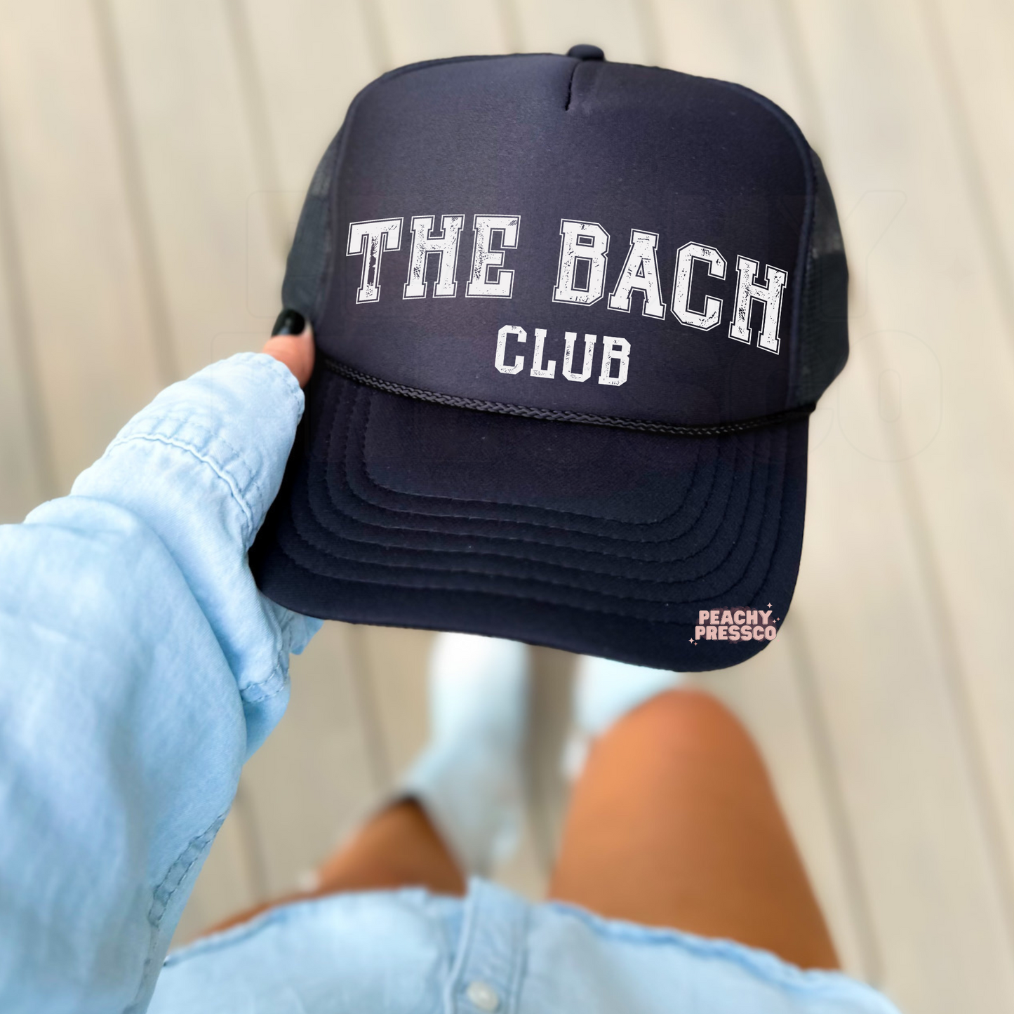 Black foam trucker hat with distressed "The Bach Club" varsity design, stylish bachelorette party hat for bridesmaids and bridal celebrations.