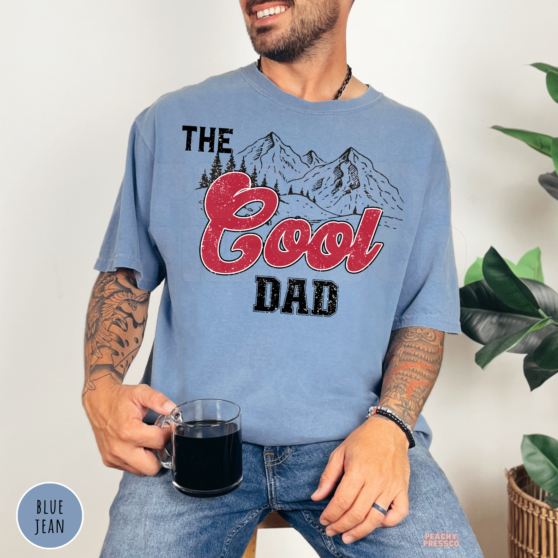 Blue Jean Comfort Colors t-shirt featuring The Cool Dad mountain graphic with distressed red lettering, a stylish Father's Day gift for dads.