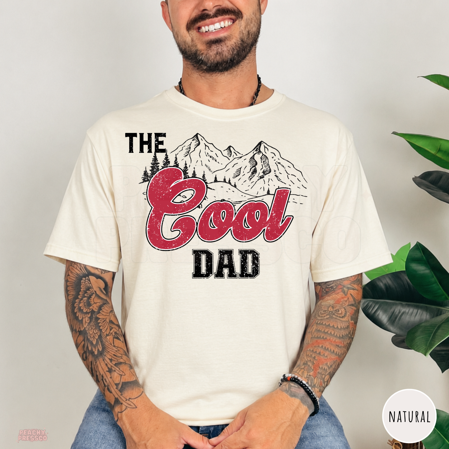 Natural t-shirt featuring The Cool Dad design with mountain scenery and distressed red lettering, a casual gift for dads.