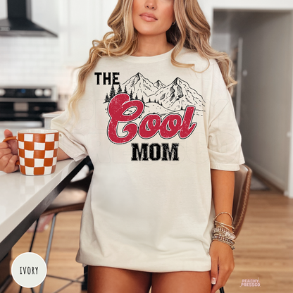 Ivory graphic t-shirt featuring a vintage "The Cool Mom" mountain design with distressed red lettering. Western-inspired mom shirt for Mother's Day and everyday wear.