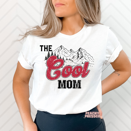 White graphic t-shirt featuring a distressed "The Cool Mom" mountain graphic with bold retro lettering. Trendy Mother's Day gift for moms who love the outdoors.