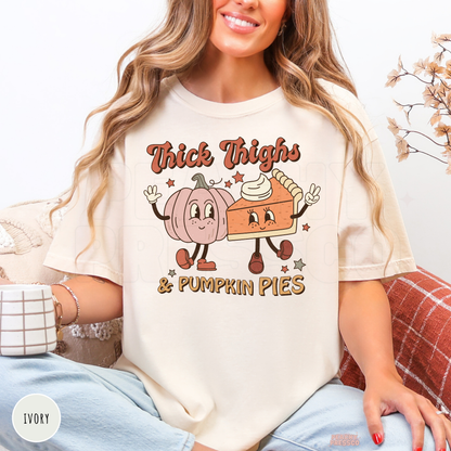 Woman wearing an ivory Comfort Colors t-shirt featuring a cute "Thick Thighs & Pumpkin Pies" graphic with a smiling pumpkin and pumpkin pie in a retro fall design.