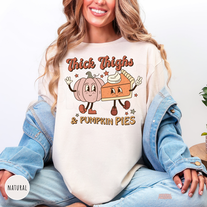 Woman wearing a natural t-shirt featuring a funny "Thick Thighs & Pumpkin Pies" graphic with retro pumpkin and pumpkin pie artwork.