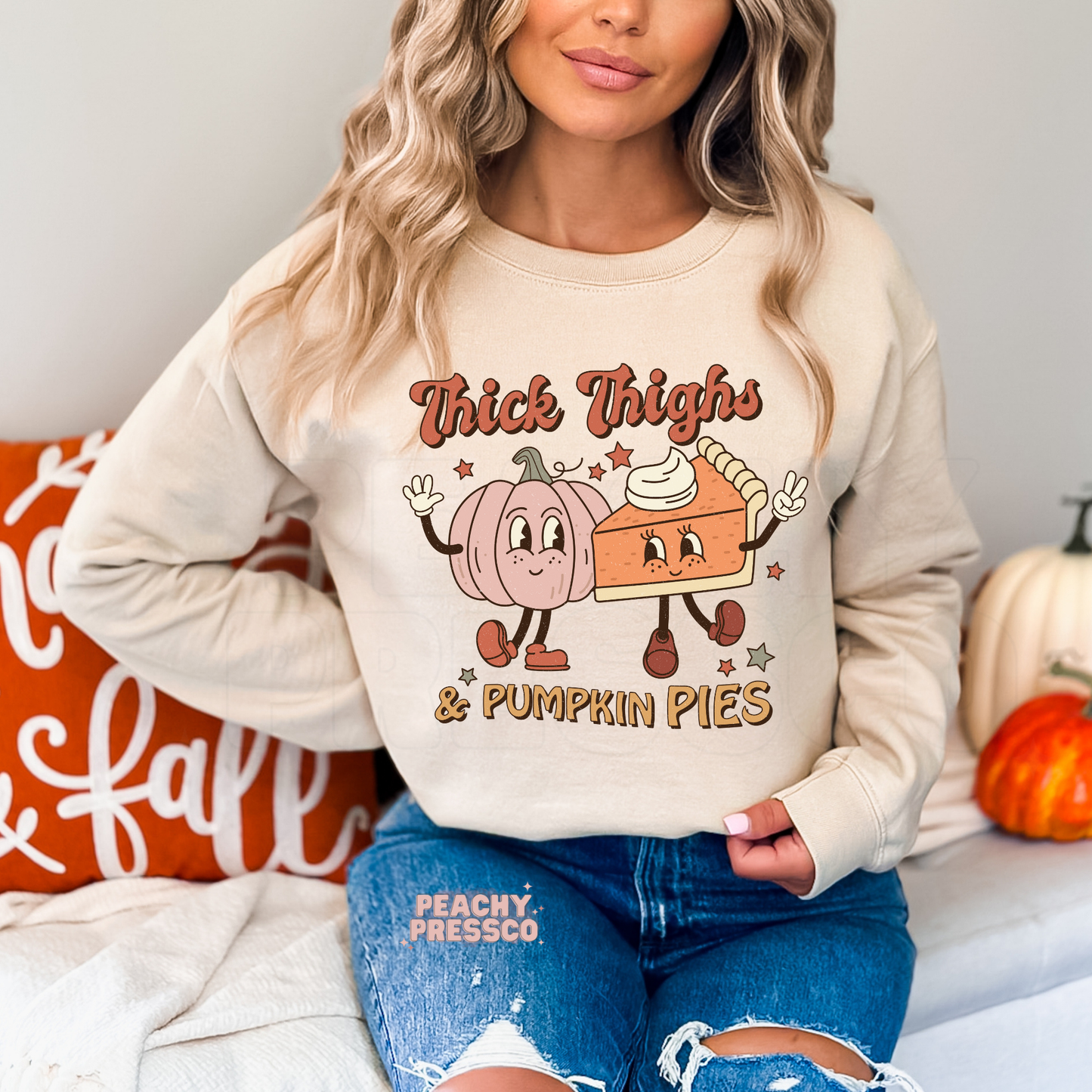 Woman wearing a sand crewneck sweatshirt with a playful "Thick Thighs & Pumpkin Pies" autumn graphic featuring adorable pumpkin and pie characters.
