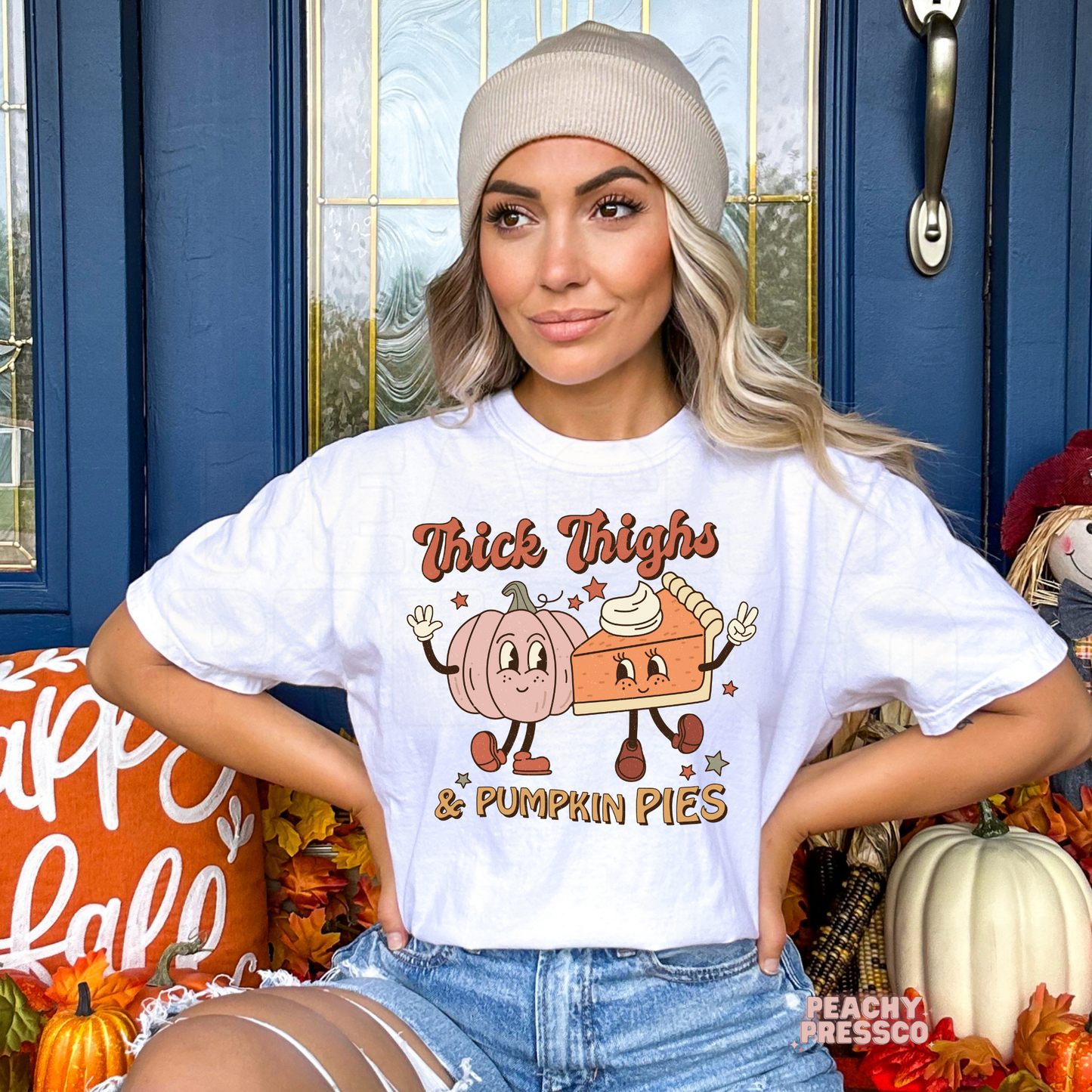 Woman wearing a white t-shirt with a vintage "Thick Thighs & Pumpkin Pies" graphic featuring smiling pumpkin and pie characters for Thanksgiving.