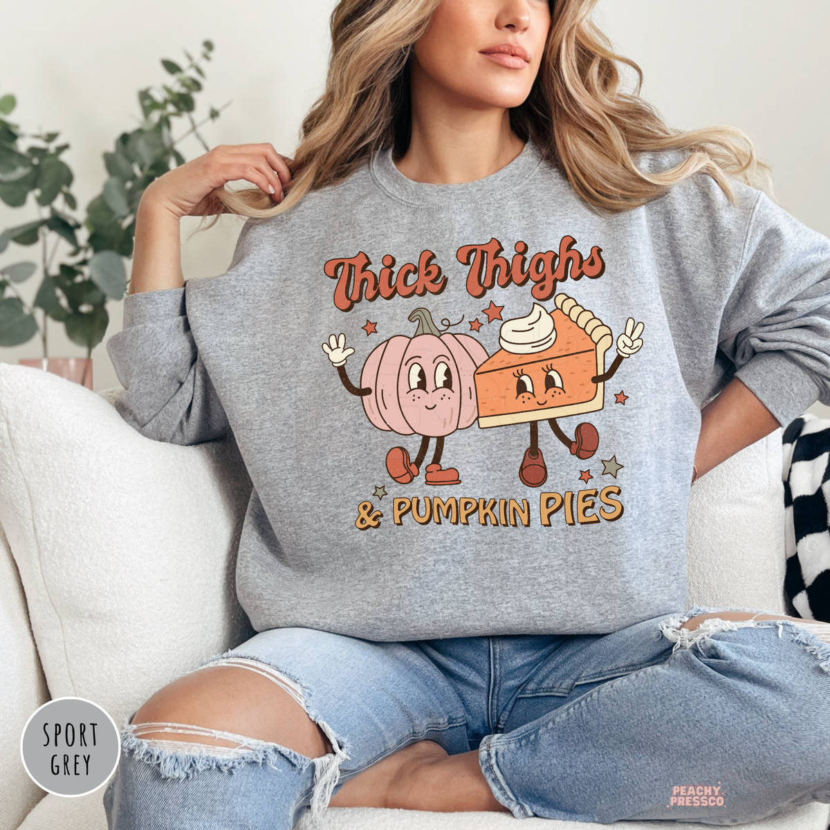 Woman wearing a sport grey crewneck sweatshirt featuring a retro "Thick Thighs & Pumpkin Pies" graphic with smiling pumpkin and pumpkin pie characters, perfect for fall and Thanksgiving.