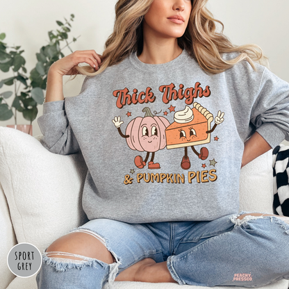 Woman wearing a sport grey crewneck sweatshirt featuring a retro "Thick Thighs & Pumpkin Pies" graphic with smiling pumpkin and pumpkin pie characters, perfect for fall and Thanksgiving.
