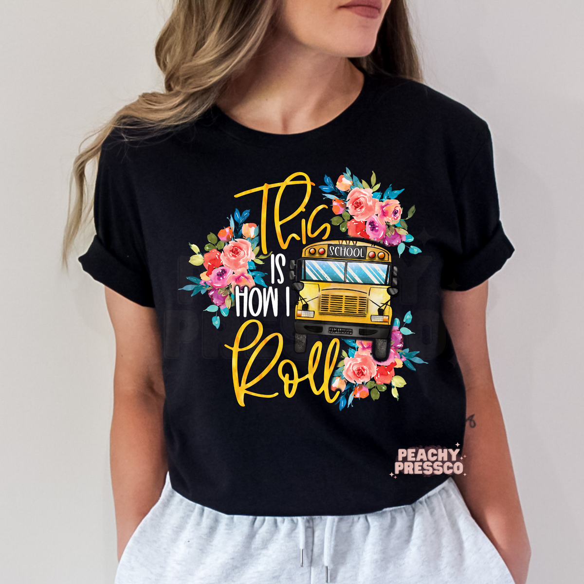 Black teacher t-shirt featuring a floral yellow school bus with "This Is How I Roll" typography and watercolor flowers.
