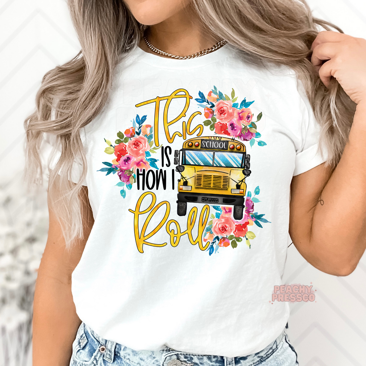 White teacher t-shirt featuring a floral school bus and "This Is How I Roll" design with colorful watercolor flowers.