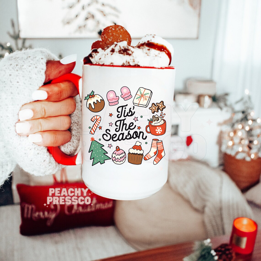 White ceramic mug with red handle printed with Tis The Season lettering surrounded by cute Christmas doodles like mittens, Christmas tree, and hot cocoa.