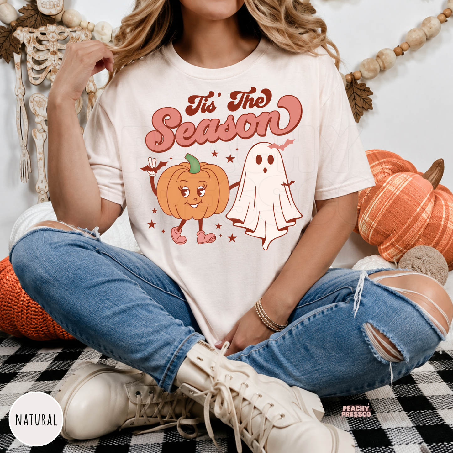 Woman wearing a natural t-shirt featuring a cute pumpkin and ghost "Tis The Season" Halloween graphic.