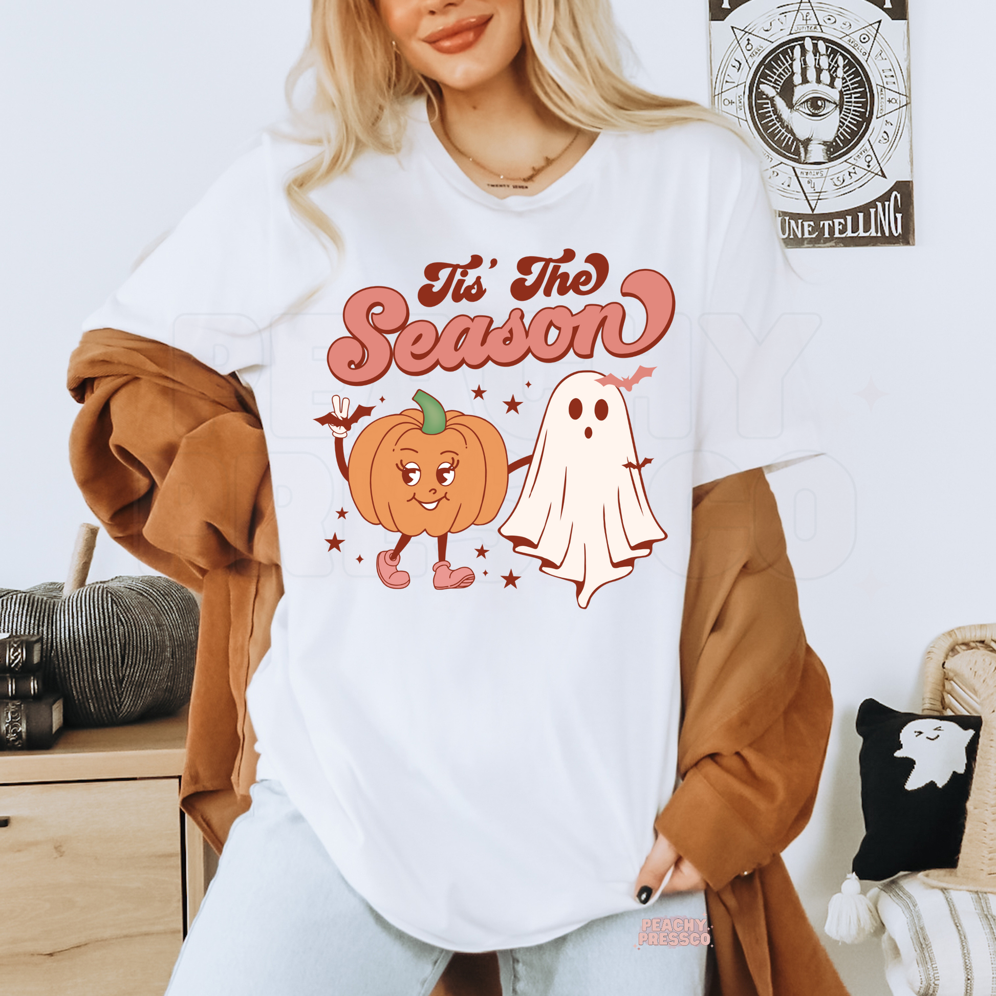 Woman wearing a white Halloween t-shirt with a retro "Tis The Season" pumpkin and ghost graphic.
