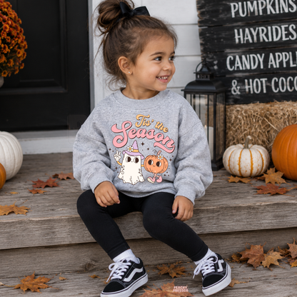 Toddler girl wearing a sport grey Tis the Season Halloween sweatshirt featuring a cute retro ghost and pumpkin design with fall pumpkins.