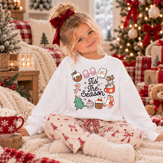 Girl wearing a white Tis the Season kids Christmas crewneck featuring festive treats, mittens and candy cane graphics